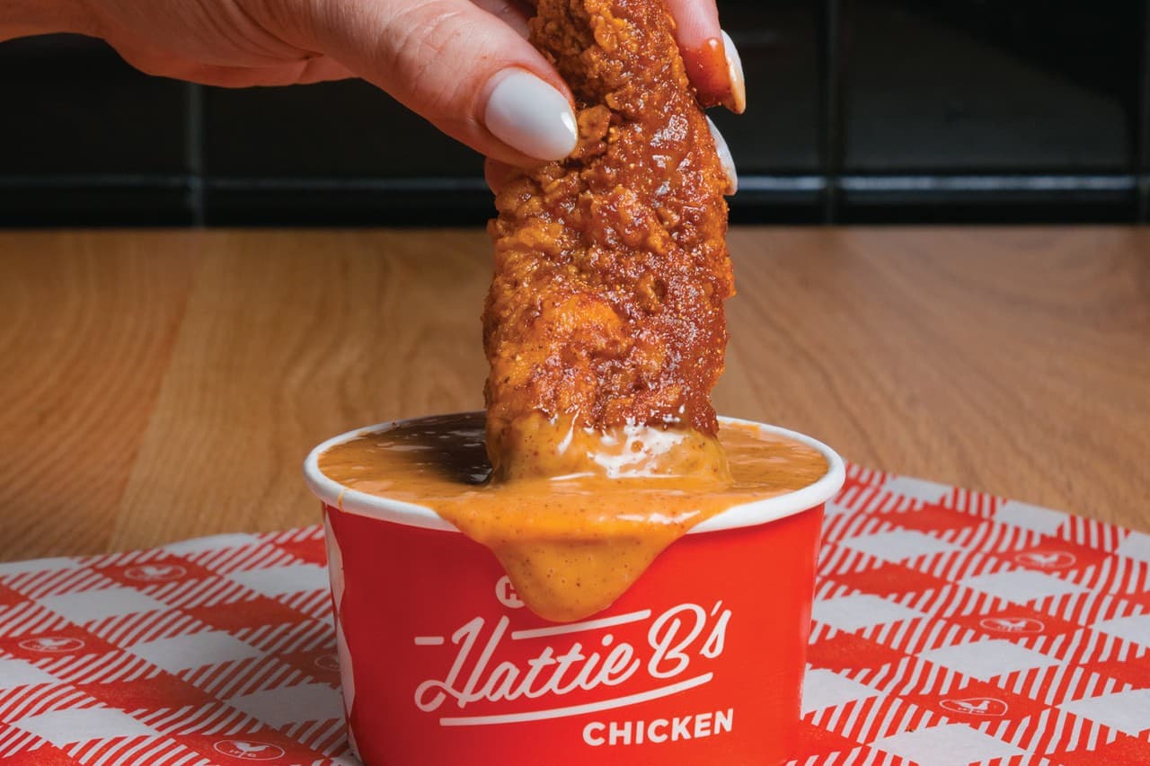 Hand dipping crispy chicken strip into sauce at the restaurant