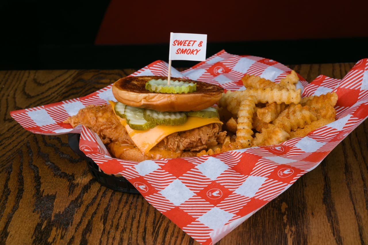 Nashville hot chicken sandwich with crispy waffle fries on checkered paper